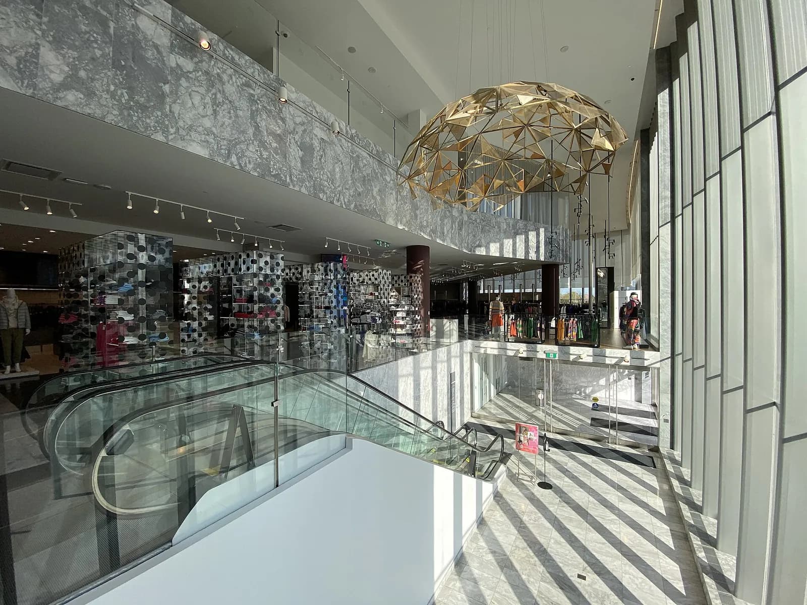 Inside Holt Renfrew at Square One in Mississauga, with escalators and a gold chandelier in the atrium